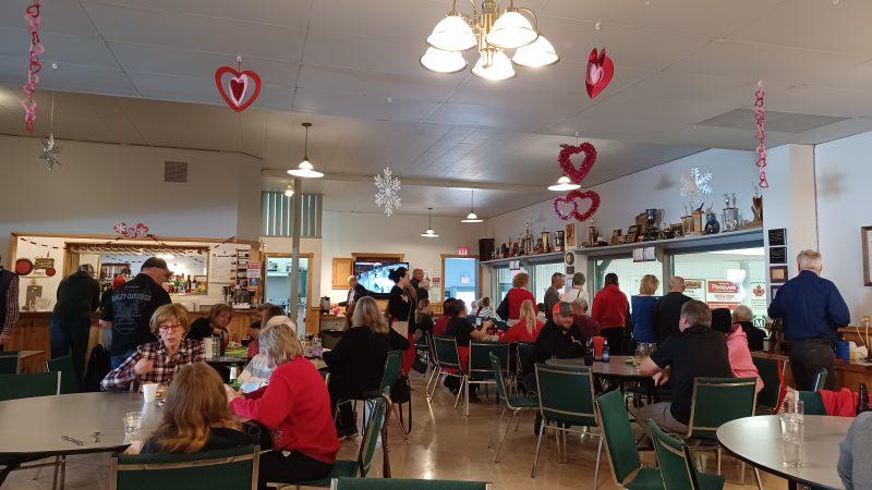 This photo was taken by journalist James Morgan. It is of a large bunch of people socializing at the Vankleek Hill Curling Club on February 11. They are sitting and standing at tables to enjoy a smoked meat sandwich while the University of Ottawa Heart Institute Bonspiel was taking place.