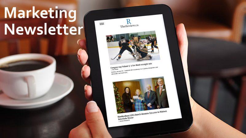 Marketing Newsletter A tablet with TheReview.ca showing on the screen that is held by a person in a cafe. The words "Marketing Newsletter" is written on the upper left corner.
