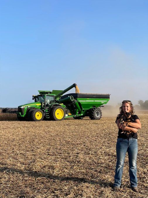 This is a photo of Sandra Clément and her dog in a cash crop field with a tractor behind them.
